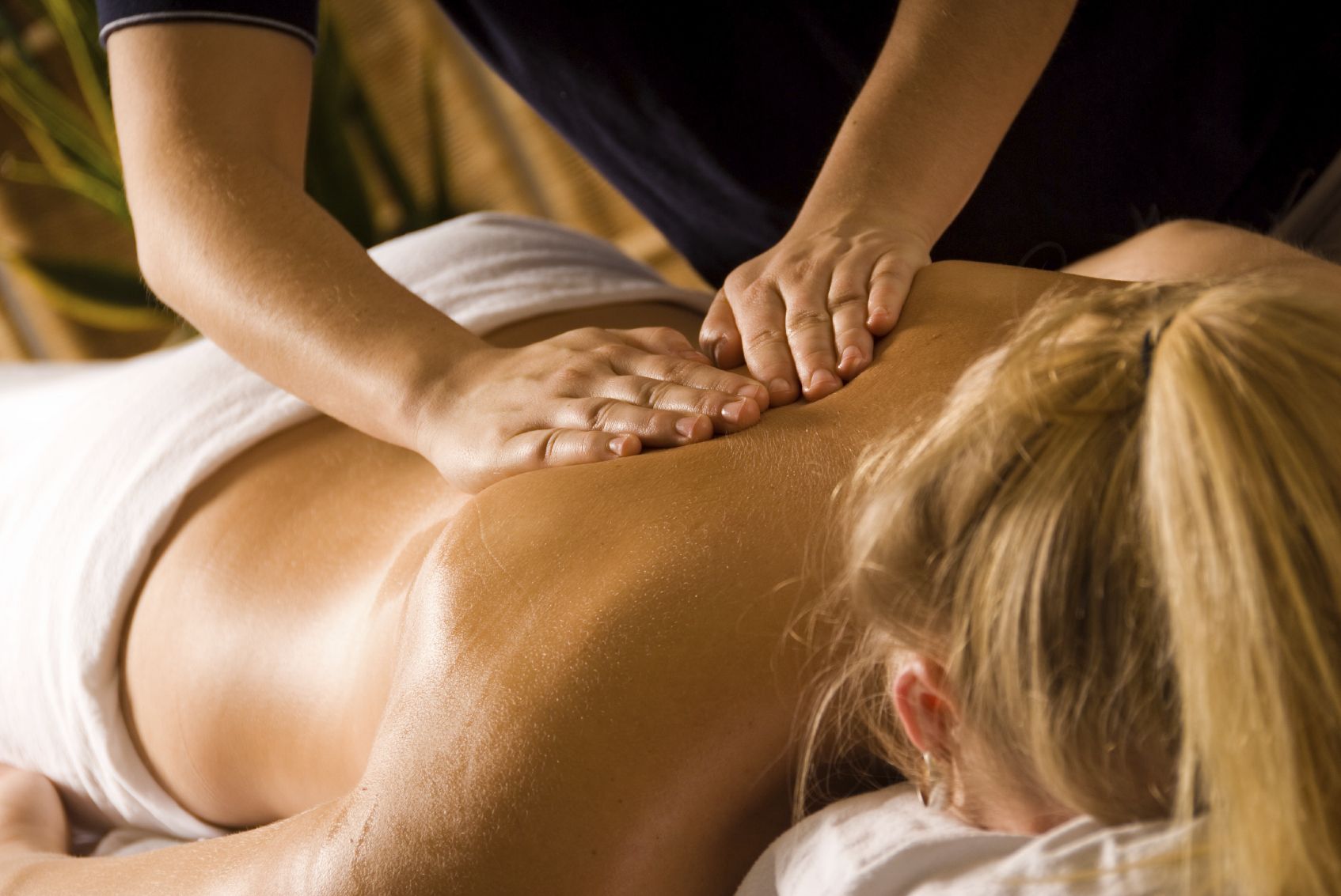 Therapist hands applying precise traditional Thai massage pressure along a client's upper back and shoulder blade in warm clinic lighting